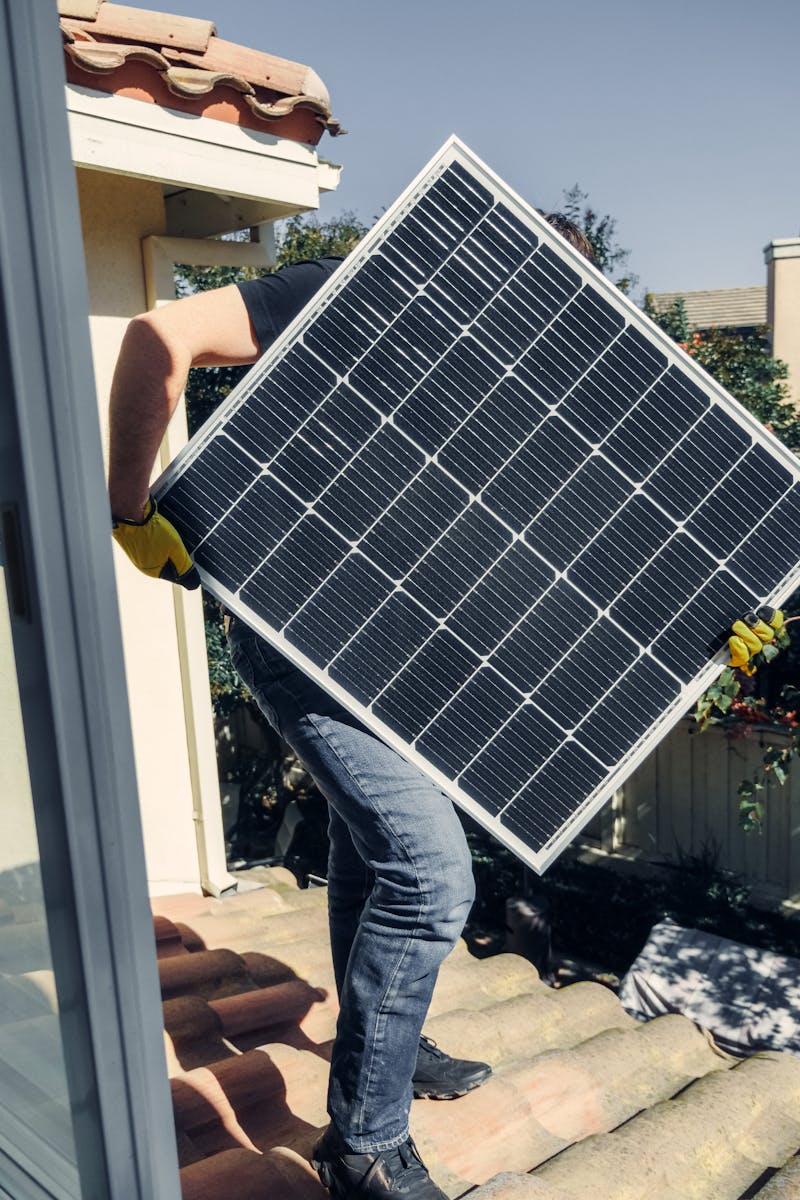 A worker carrying a solar panel for installation on a sunlit rooftop, showcasing clean energy.